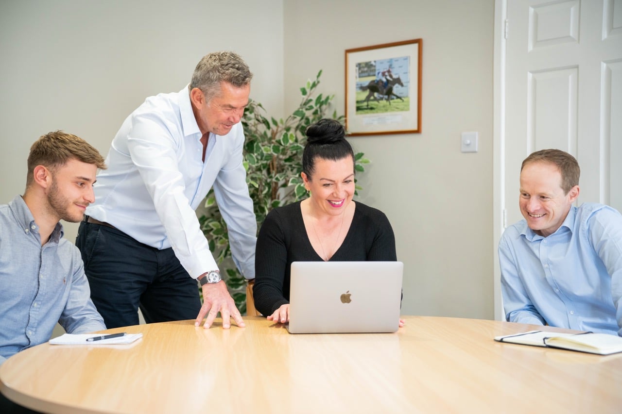 people stood around a desk looking at laptop